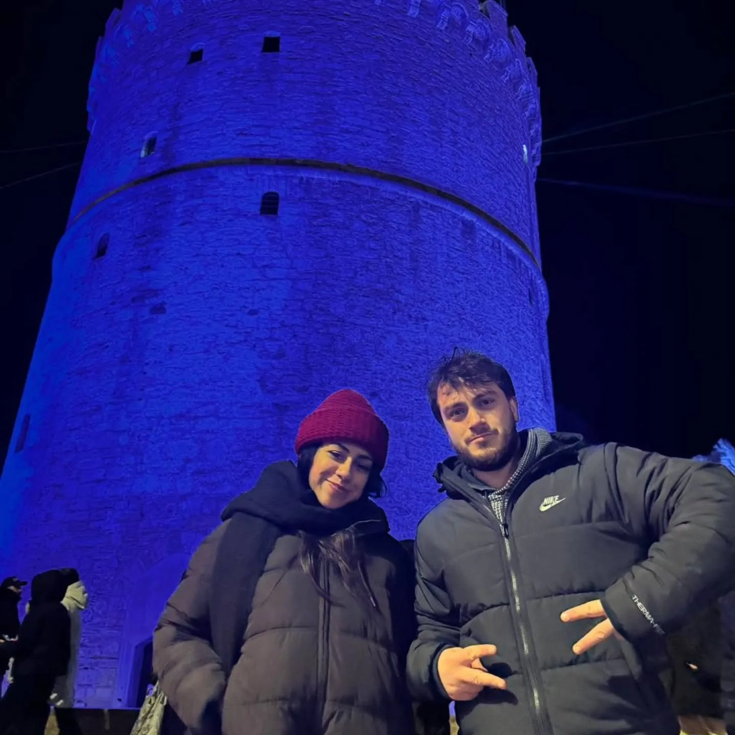 Michalis and Cristal in front of a blue-lit stone tower at night